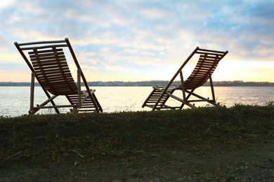 Photo of Empty wooden deckchairs on hill near calm river