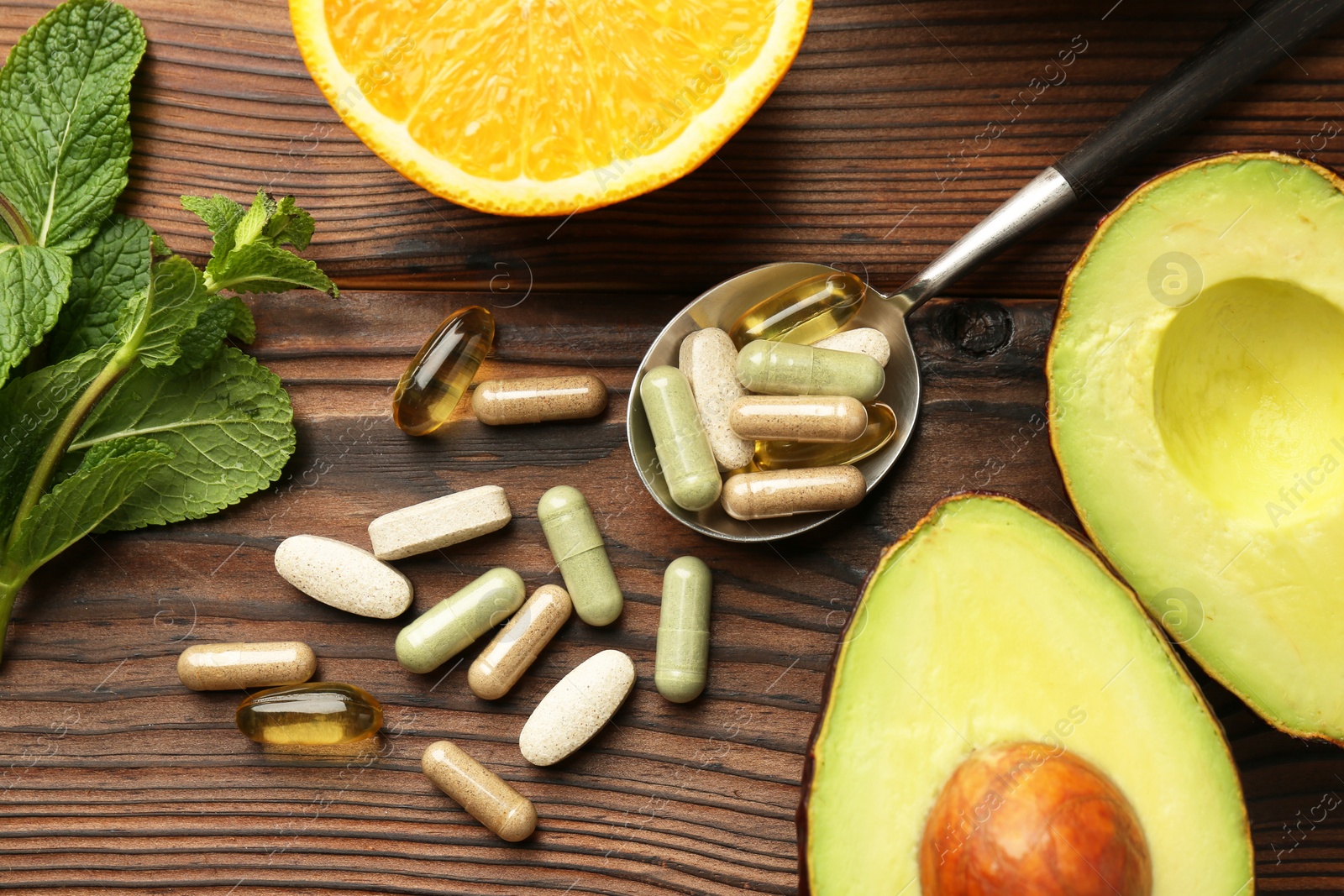 Photo of Different vitamin pills, avocado, orange and mint on wooden table, flat lay