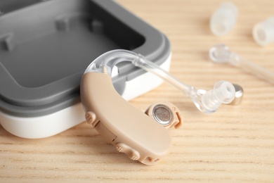 Hearing aid and case on wooden table, closeup