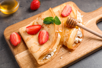 Photo of Delicious thin pancakes with strawberries, cottage cheese and honey on grey table, closeup