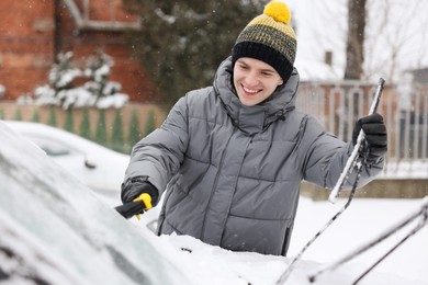 Man cleaning snow from car windshield outdoors