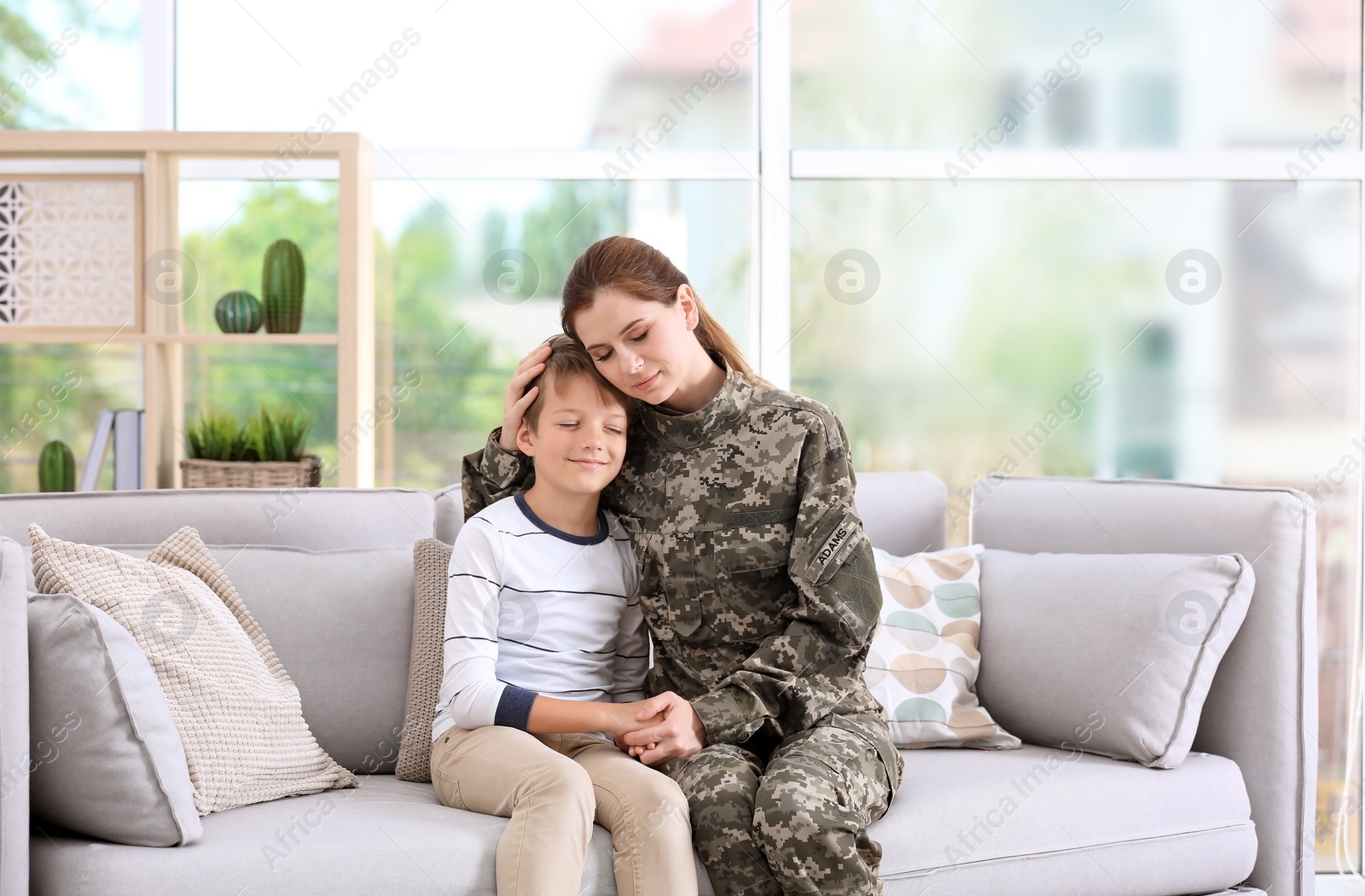 Photo of Woman in military uniform with her little son on sofa at home