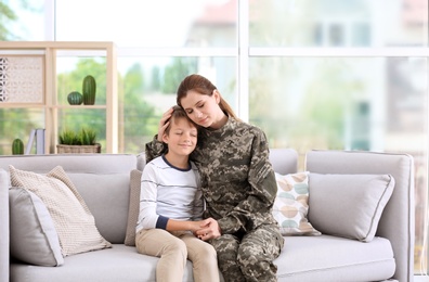 Woman in military uniform with her little son on sofa at home