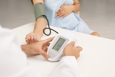 Photo of Young doctor checking pregnant woman's blood pressure in hospital. Patient consultation