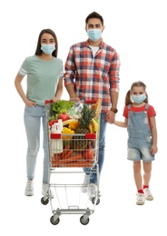 Family in medical masks with shopping cart full of groceries on white background