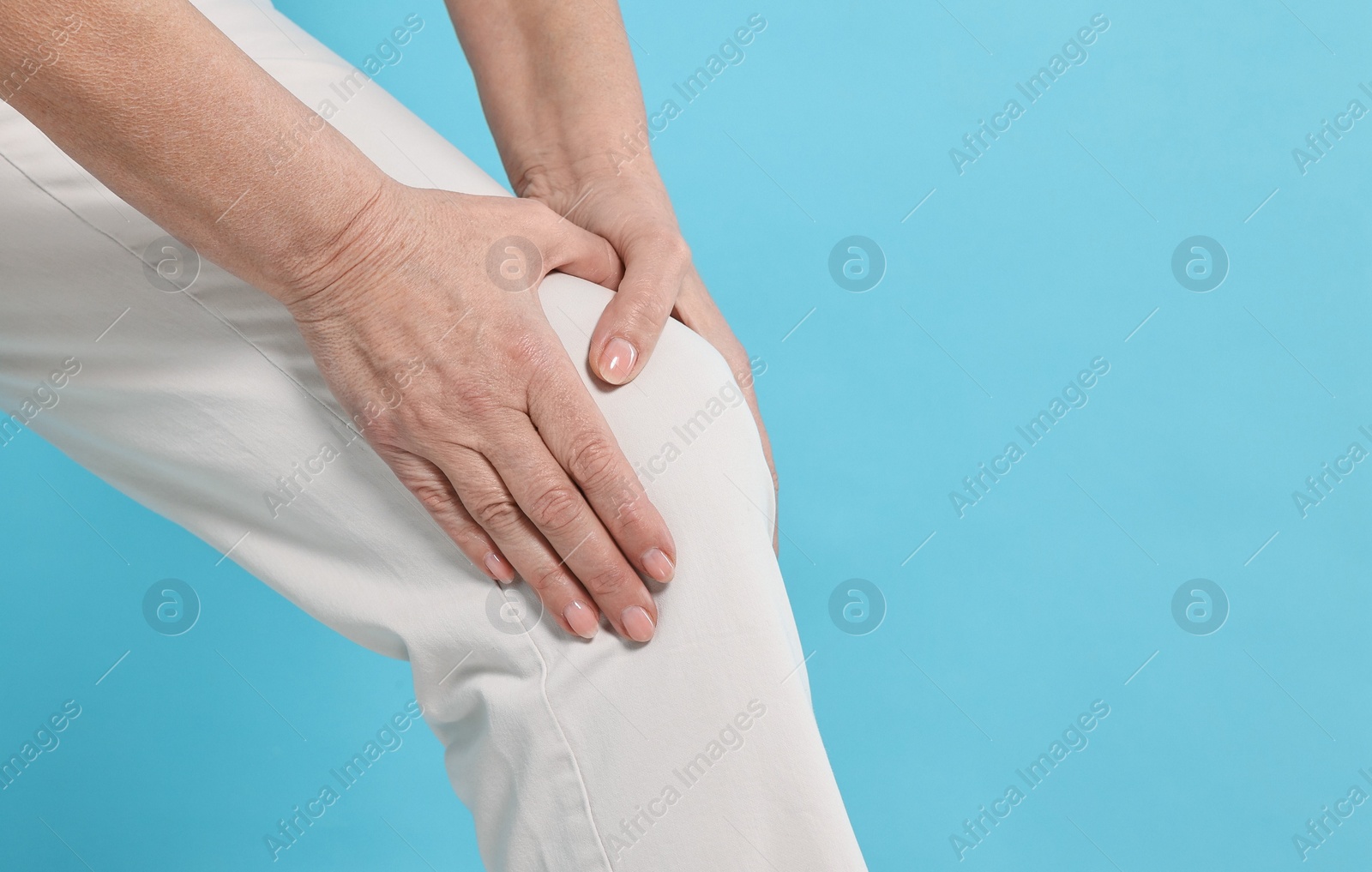 Photo of Arthritis symptoms. Woman suffering from pain in knee on light blue background, closeup