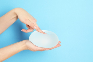 Photo of Woman touching silicone implant for breast augmentation on color background, space for text. Cosmetic surgery