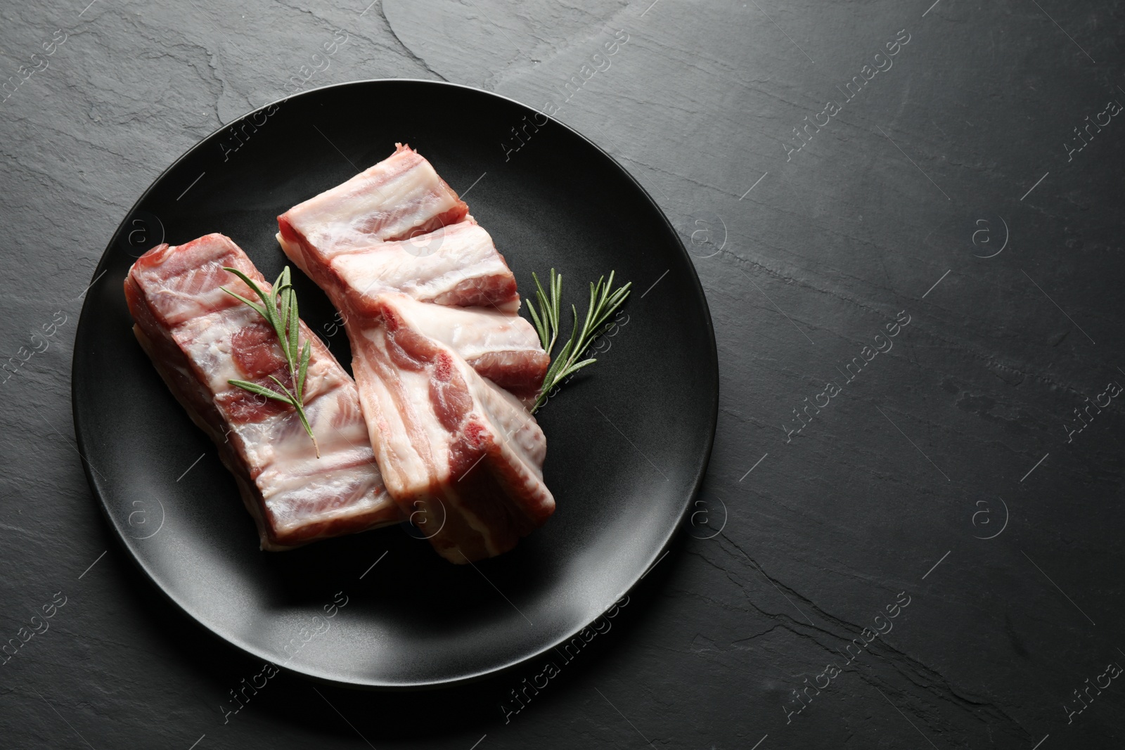 Photo of Raw ribs with rosemary on black table, top view