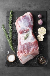 Photo of Piece of raw pork belly, rosemary, garlic and spices on grey textured table, top view