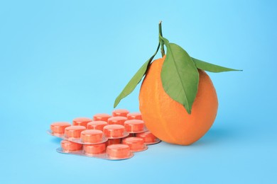 Photo of Fresh orange and blisters with cough drops on light blue background