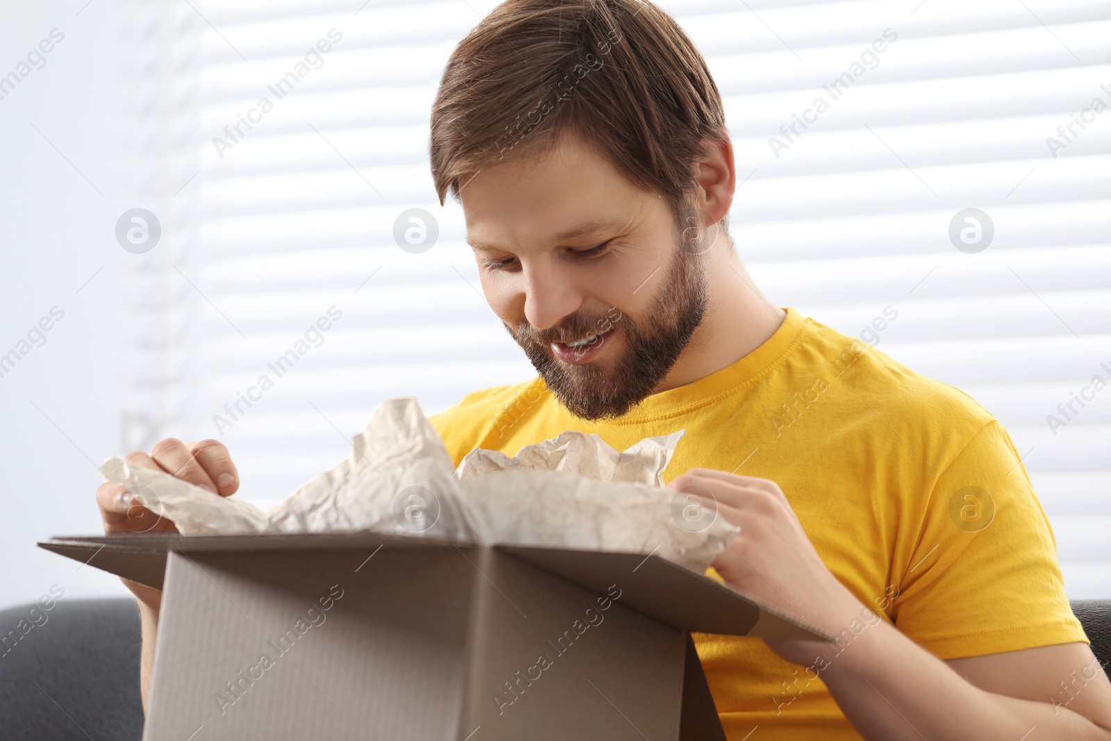 Photo of Happy man opening parcel at home. Internet shopping