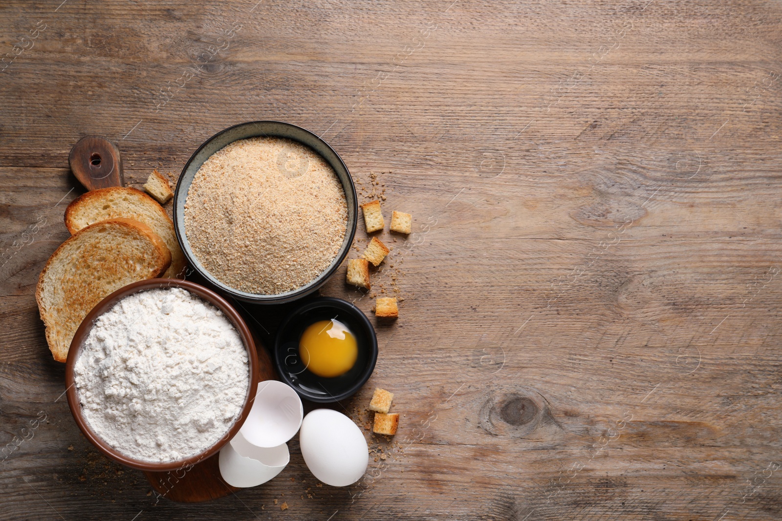 Photo of Fresh breadcrumbs, flour and eggs on wooden table, flat lay. Space for text