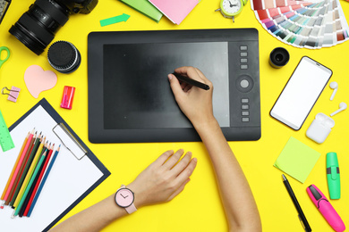 Photo of Professional designer drawing with graphic tablet at yellow table, top view