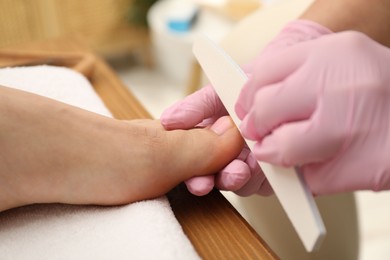 Photo of Professional pedicurist filing client`s toenails in beauty salon, closeup