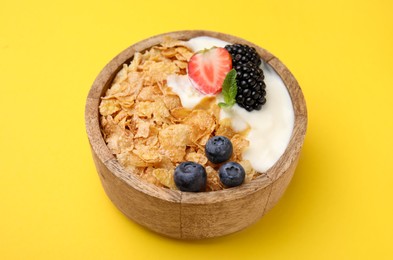 Photo of Delicious crispy cornflakes, yogurt and fresh berries in bowl on yellow background, closeup. Healthy breakfast