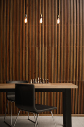 Modern table with chess near wooden wall