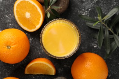Photo of Tasty fresh oranges, juice, stones and leaves on black table, flat lay