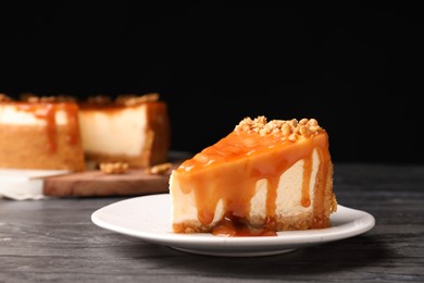 Photo of Piece of delicious cake with caramel and walnuts on black table