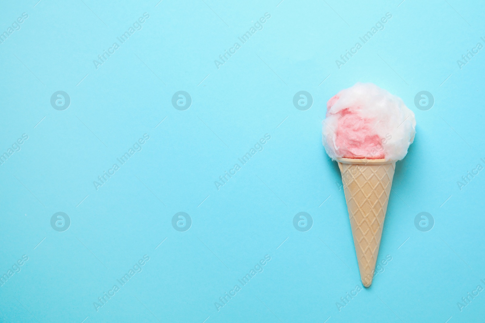 Photo of Ice cream cone with fluffy cotton candy and space for text on color background, top view