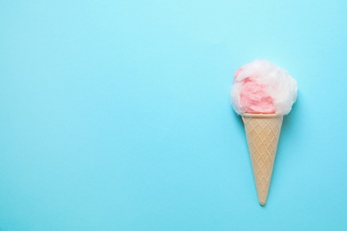 Photo of Ice cream cone with fluffy cotton candy and space for text on color background, top view