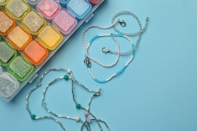 Photo of Beautiful handmade beaded jewelry and supplies on light blue background, flat lay