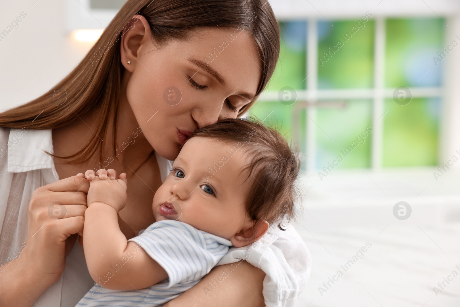 Photo of Happy mother kissing her little baby in kitchen. Space for text