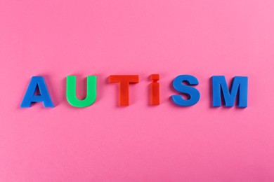 Photo of Word Autism made with colorful letters on pink background, top view