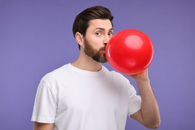 Photo of Man inflating red balloon on purple background