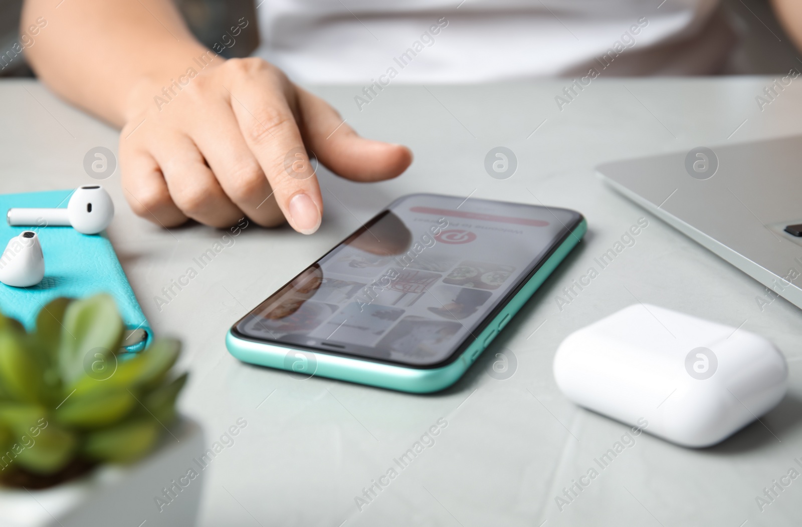 Photo of MYKOLAIV, UKRAINE - JULY 10, 2020: Woman using with Pinterest app on Iphone 11 at table, closeup
