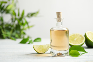 Photo of Lime essential oil and cut fruits on white wooden table. Space for text