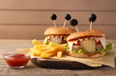 Photo of Cute monster burgers served with french fries and ketchup on wooden table. Halloween party food