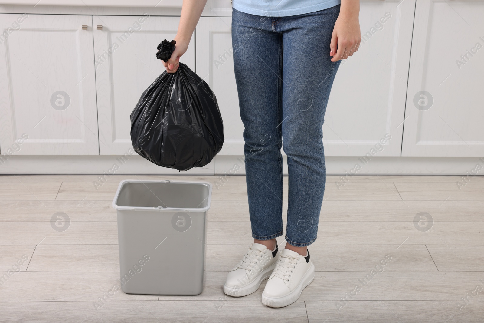 Photo of Woman taking garbage bag out of trash bin in kitchen, closeup