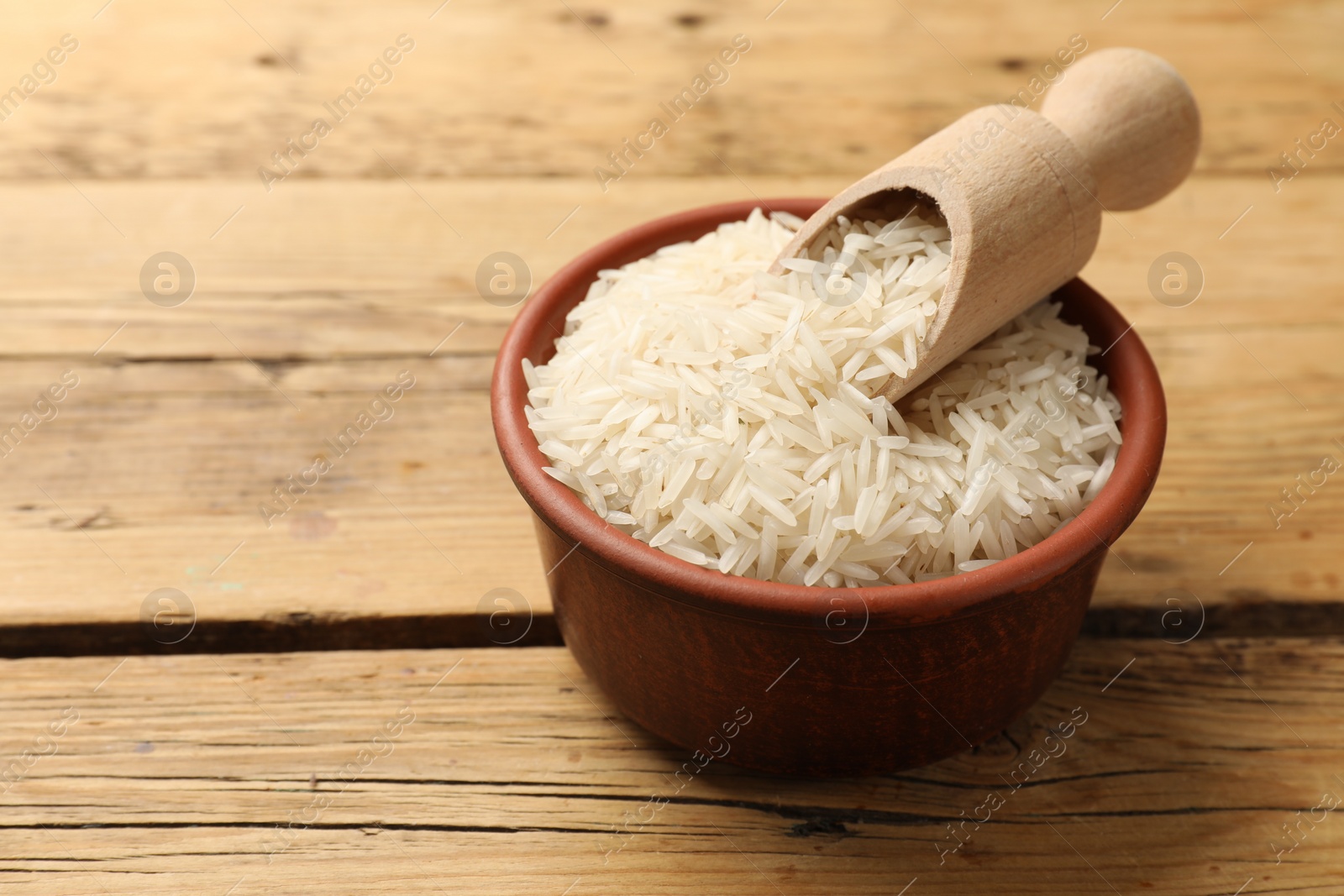 Photo of Raw basmati rice and scoop in bowl on wooden table. Space for text