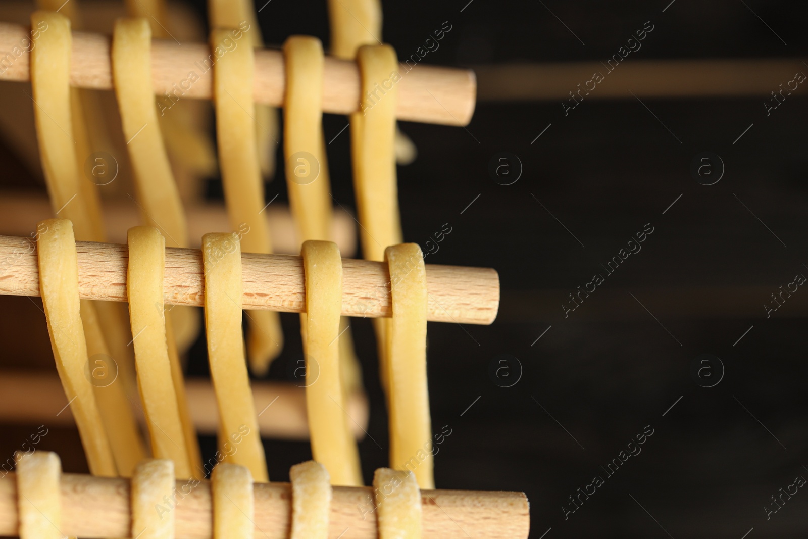 Photo of Homemade pasta drying on wooden rack against dark background, closeup. Space for text