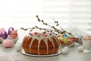 Delicious Easter cake decorated with sprinkles near painted eggs on white wooden table
