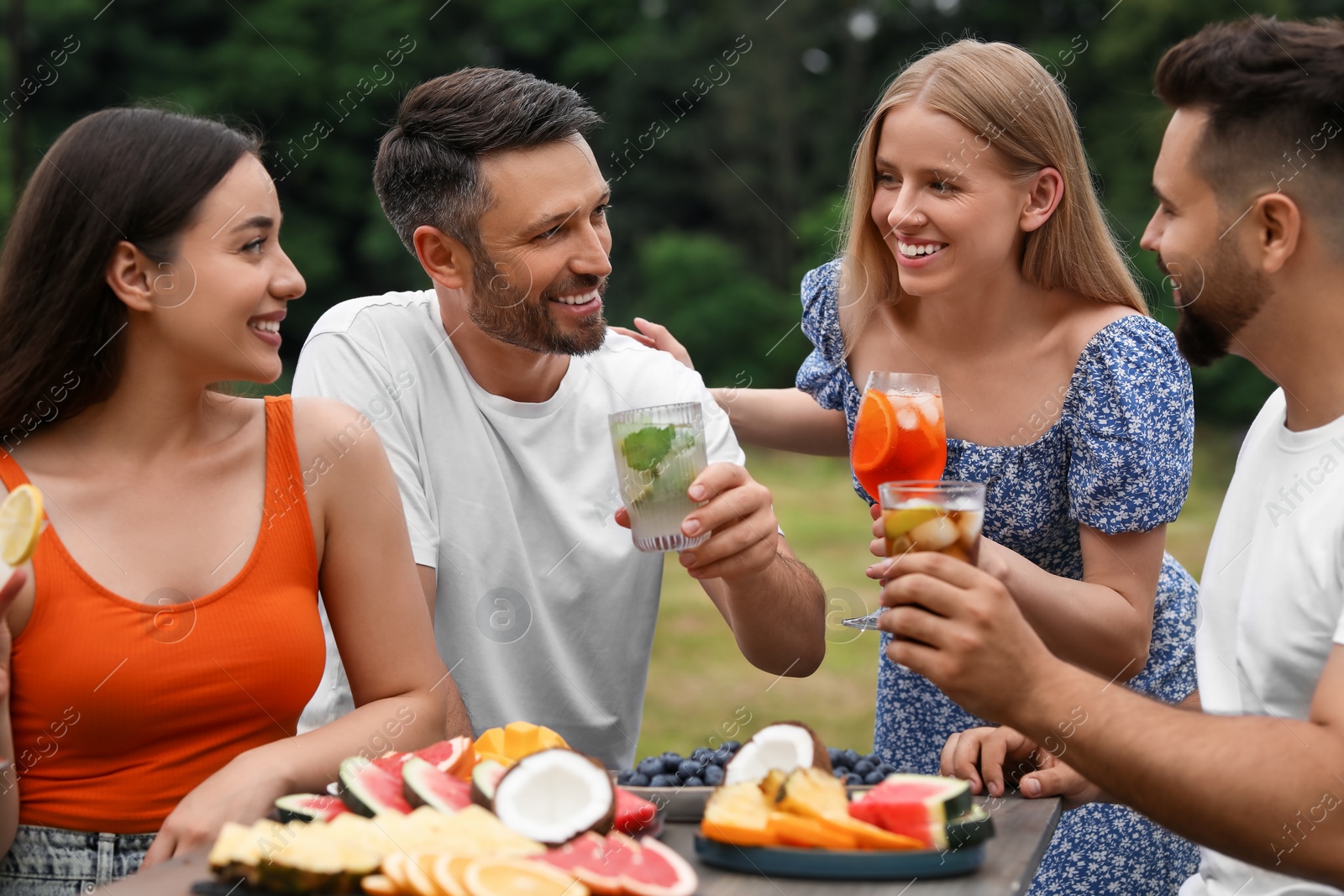 Photo of Happy friends with glasses of cocktails at table outdoors