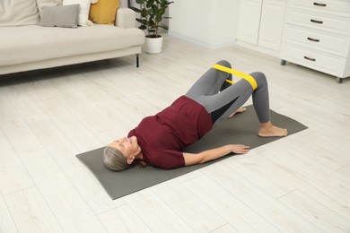 Photo of Senior woman doing exercise with fitness elastic band on mat at home