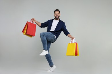 Photo of Happy man with many paper shopping bags dancing on grey background