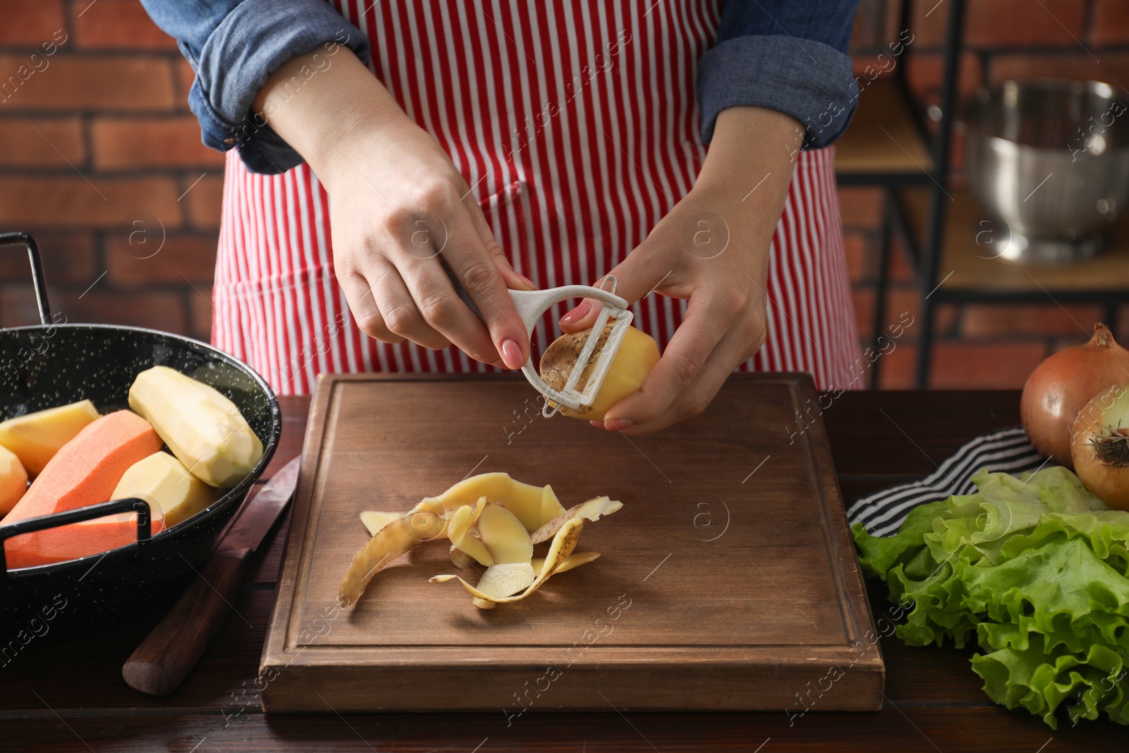 Photo of Woman peeling fresh potato at wooden table indoors, closeup