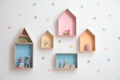 Stylish house shaped shelves with toys on white wall. Baby room interior design
