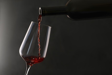 Pouring red wine from bottle into glass on dark background. Space for text