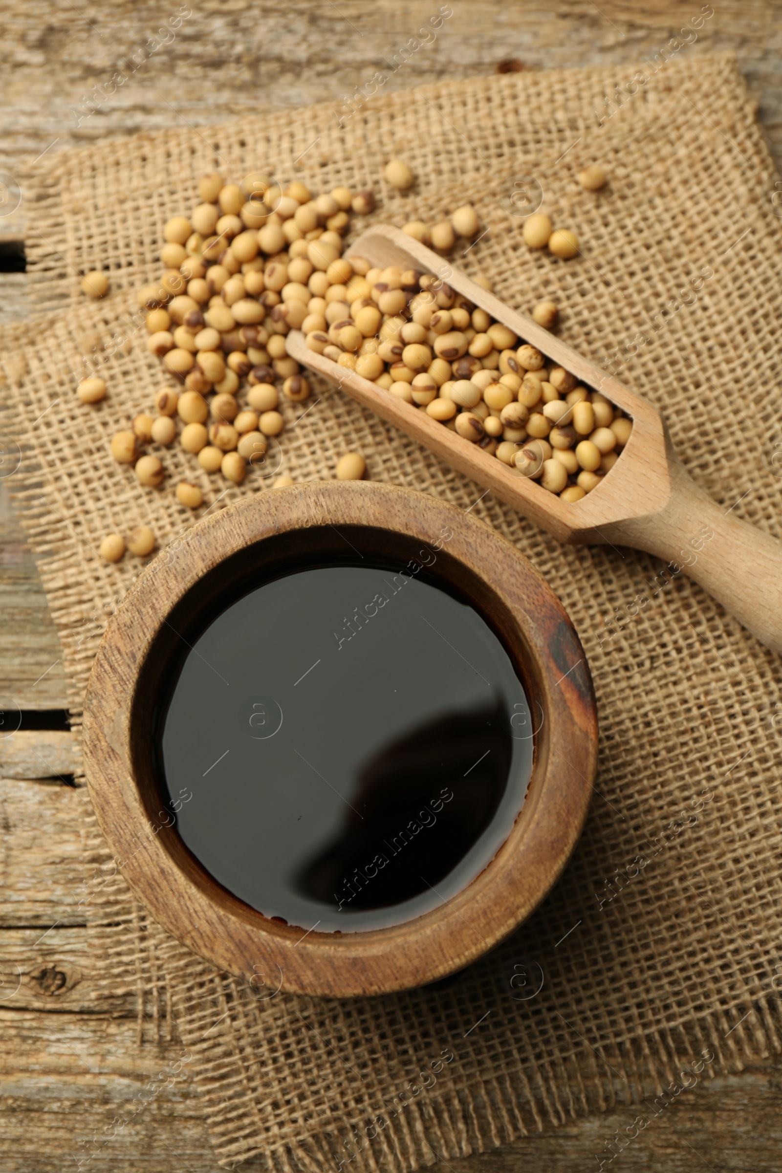 Photo of Soy sauce in bowl and soybeans on wooden table, flat lay