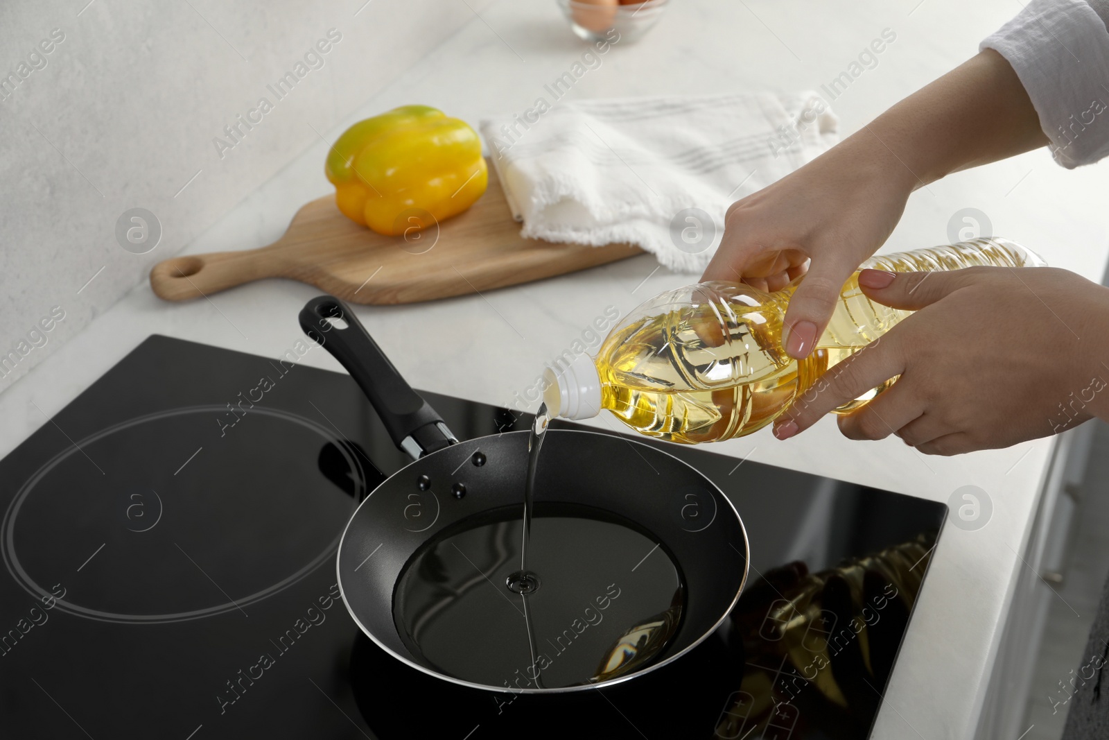 Photo of Woman pouring cooking oil from bottle into frying pan on stove, closeup