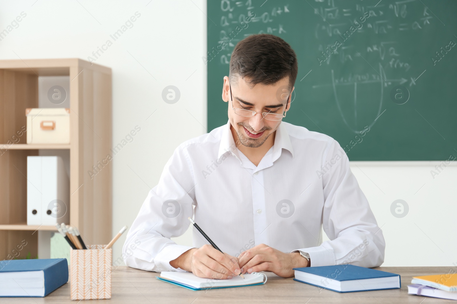 Photo of Young male teacher working at table in classroom