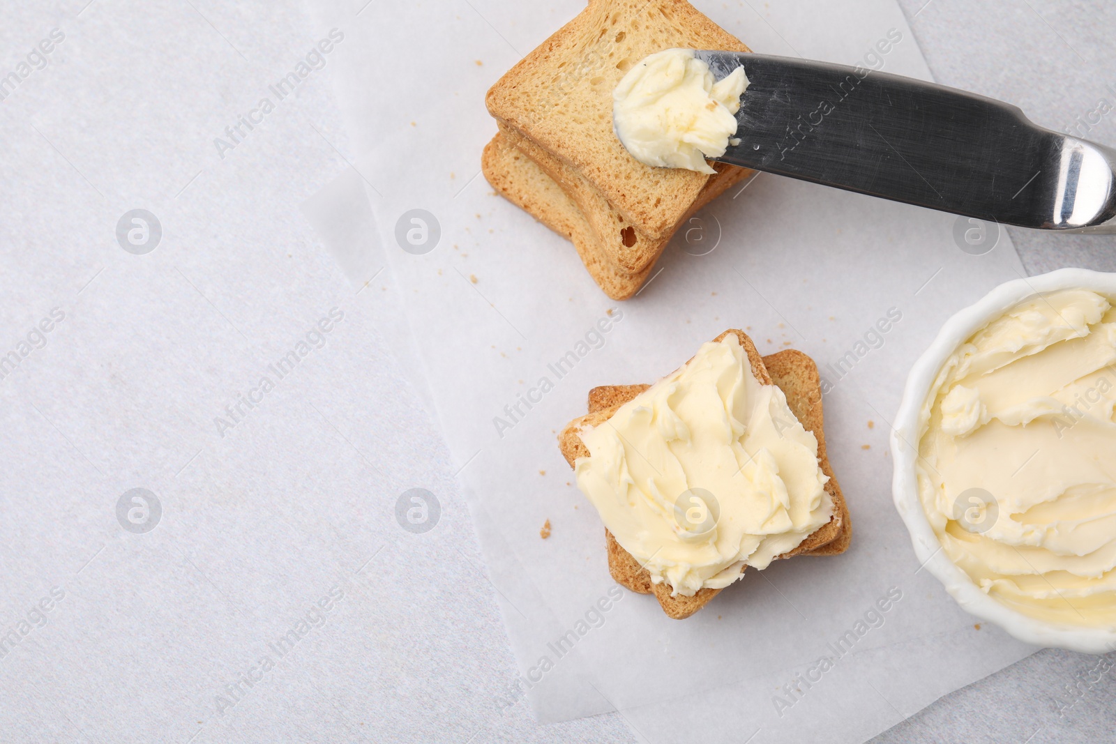 Photo of Slices of bread with tasty butter and knife on light gray table, flat lay. Space for text