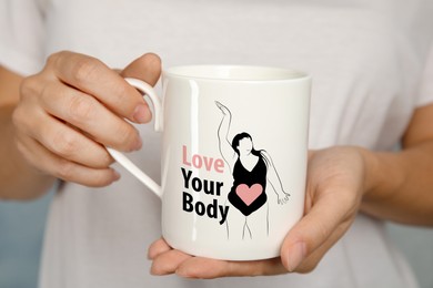 Image of Woman holding cup with image of figure of plus-size model in bodysuit, heart and phrase Love Your Body, closeup