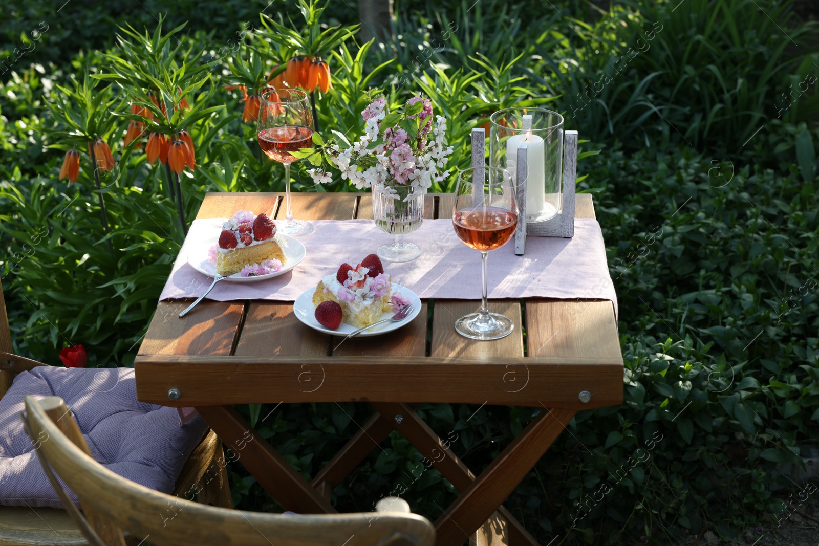 Photo of Vase with spring flowers, wine and cake on table served for romantic date in garden