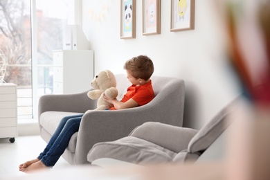 Little autistic boy sitting on sofa with toy at home