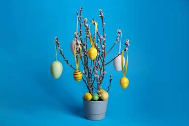 Photo of Beautiful willow branches with painted eggs in pot on light blue background. Easter decor