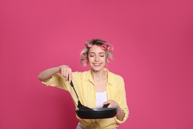 Photo of Young housewife with frying pan and spatula on pink background